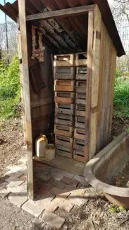 a picture of an old shed with a tin roof with it's wooden door open showing two stacks of traditional wooden fruit boxes inside